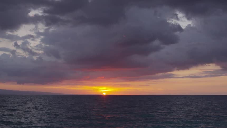The sun sets on the horizon of the ocean on a cloudy evening
