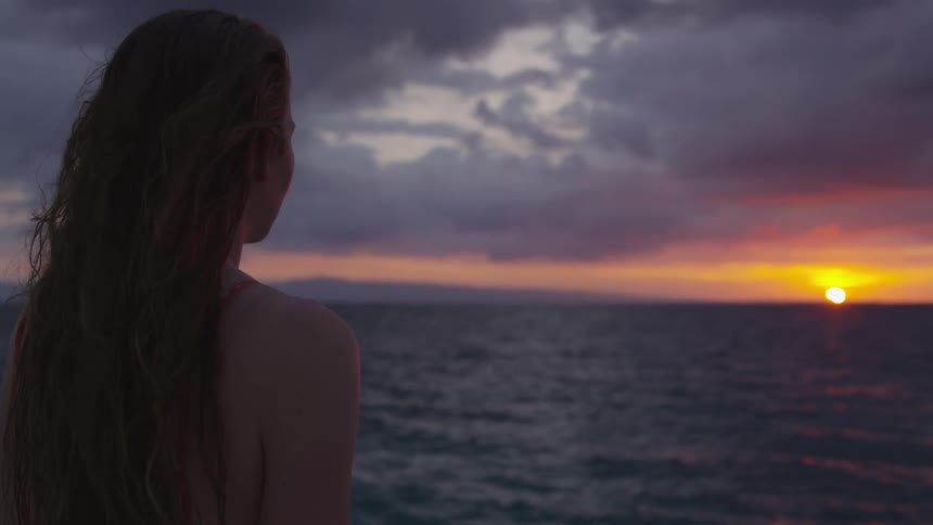 A woman watches the sun set on the beach