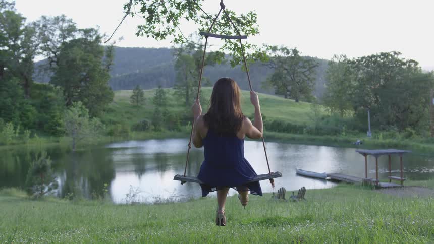 Woman sits on tree swing near pond