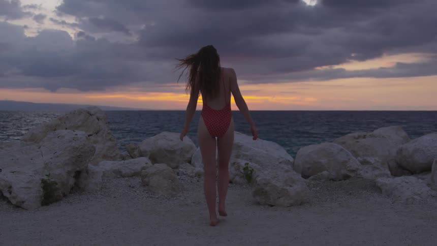A woman wearing a bathing suit walking on a boulder covered beach