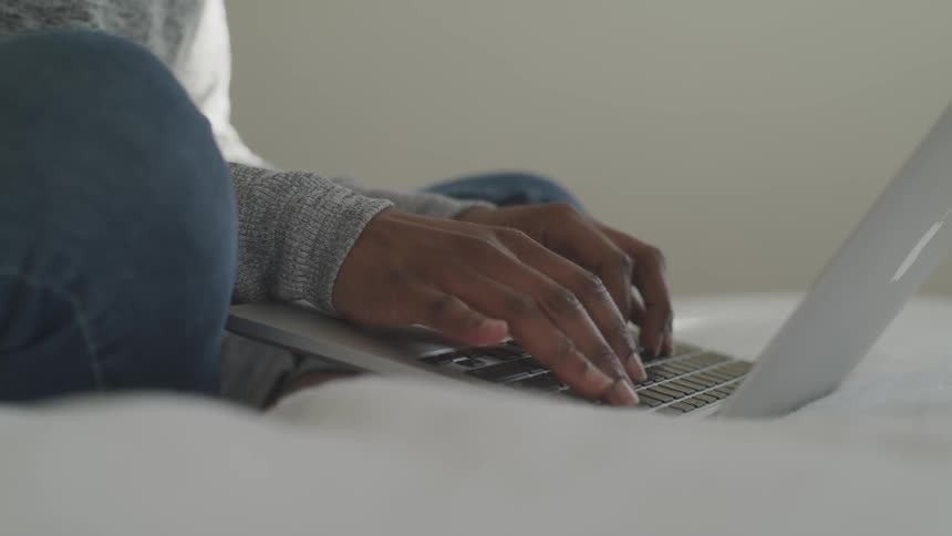 A woman on a bed typing on a laptop