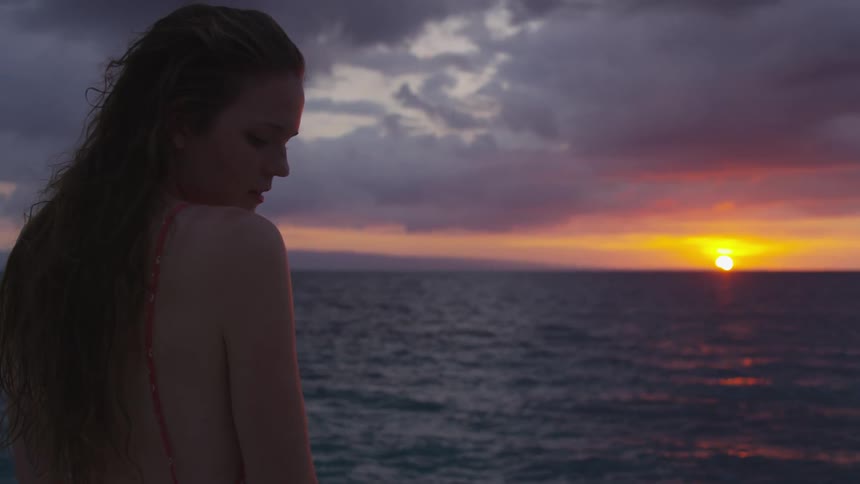A woman standing near the ocean during sunset