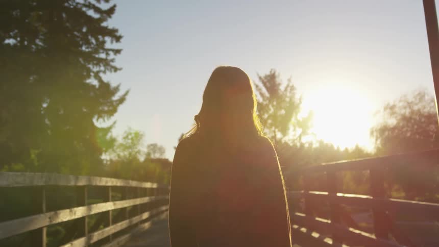 Woman stands on a bridge with the sun in the background