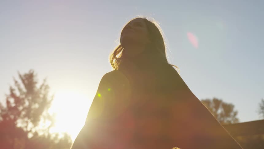 A young white woman looks into the sky as she spins in a circle with her arms stretched out at her sides