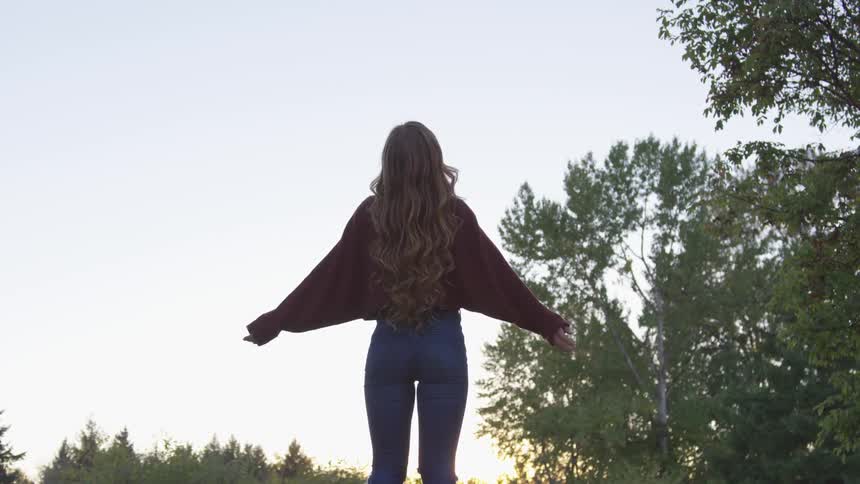 Woman lifts her arms to the sky at sunset