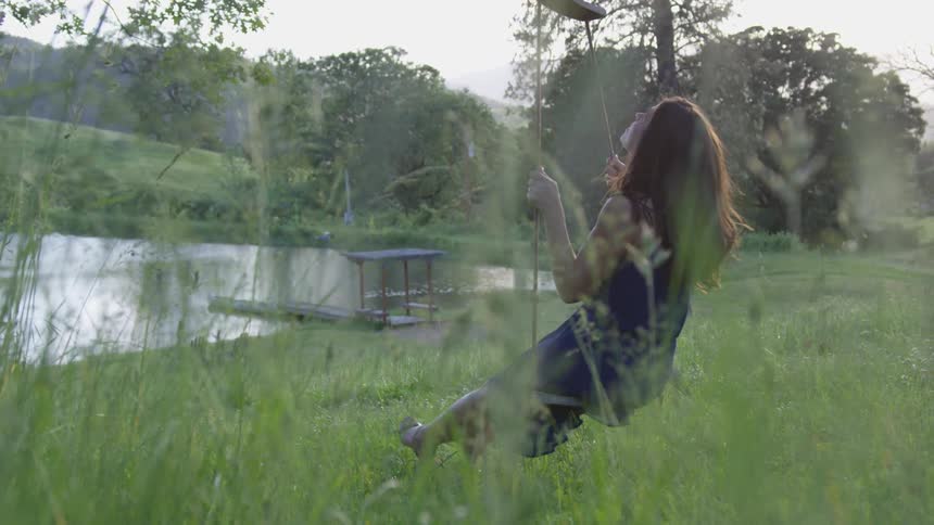 A woman on a swing in the tall grass by a lake
