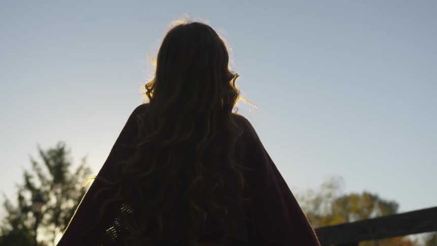 Woman wearing poncho spins around under sky