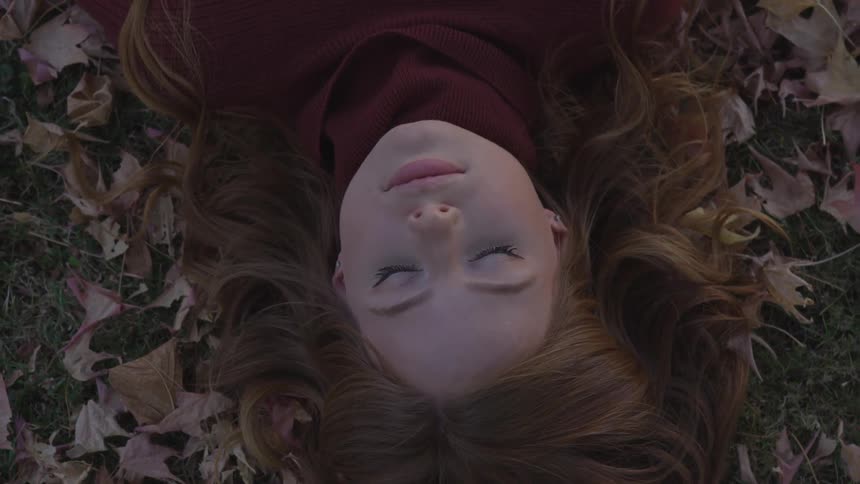 A woman lays down on the grass with her eyes closed