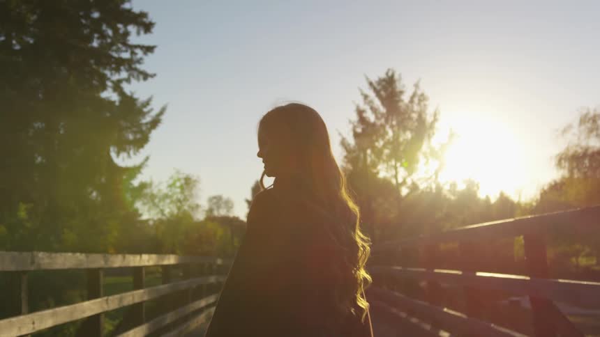 A brunette woman walks across a wooden bridge