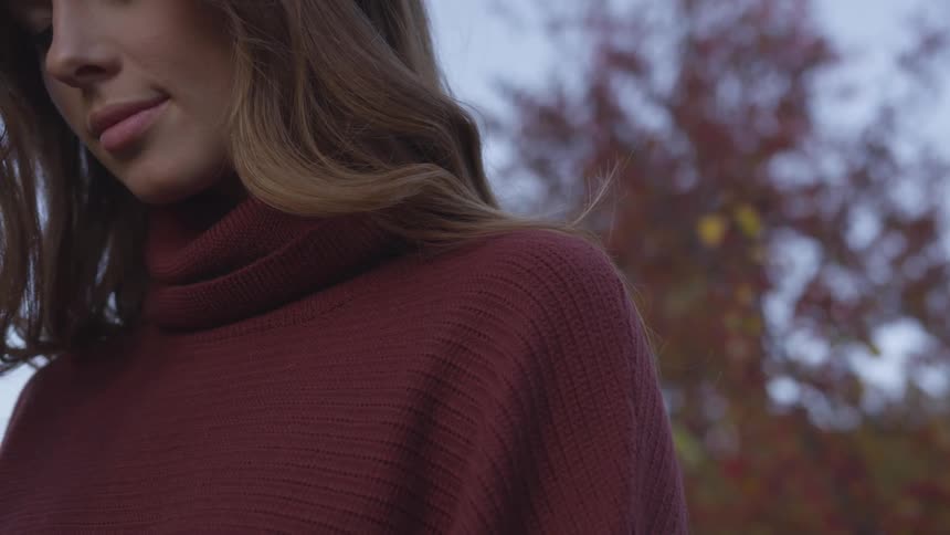 A woman stands in front of fall trees