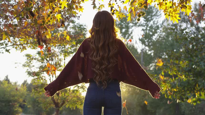 A woman is outdoors and leaves are falling