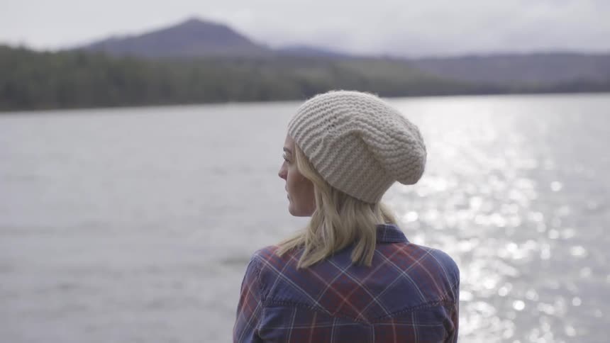 A woman stands by a lake on a cloudy day