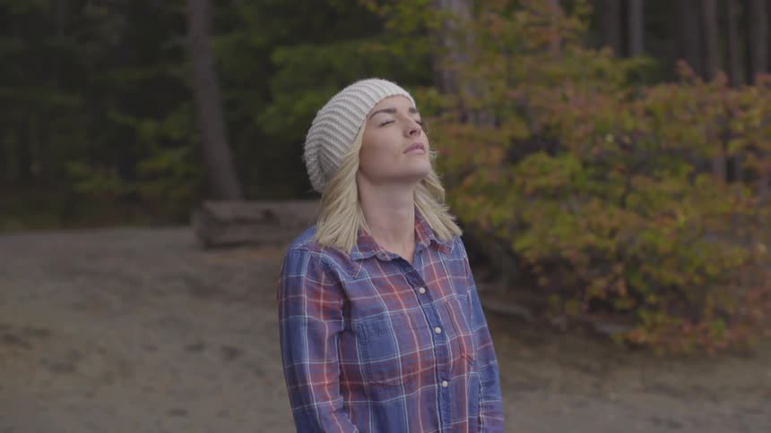 A young woman stands with her eyes closed in a wooded area