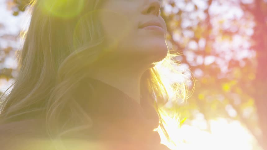A woman stands in front of the sun in a park in the fall
