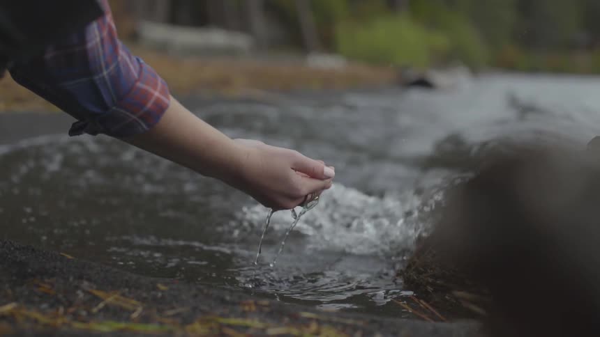 Woman scoops some water from the lake with her hands
