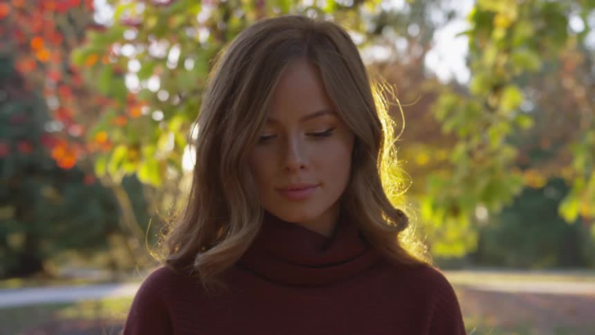 Woman looks down while standing under trees