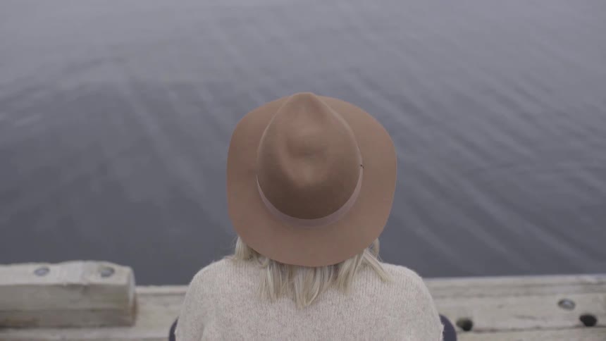 A blonde woman is seated on a pier next to a lake