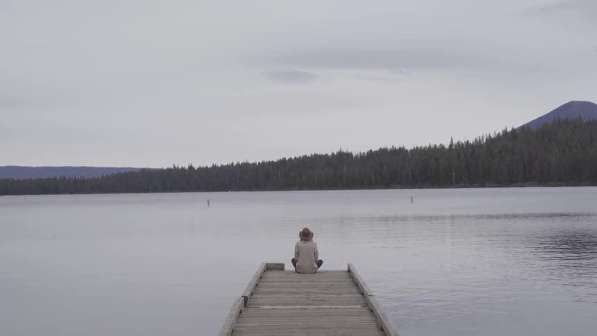 Person in sun hat sits at the end of a pier and stares into distance
