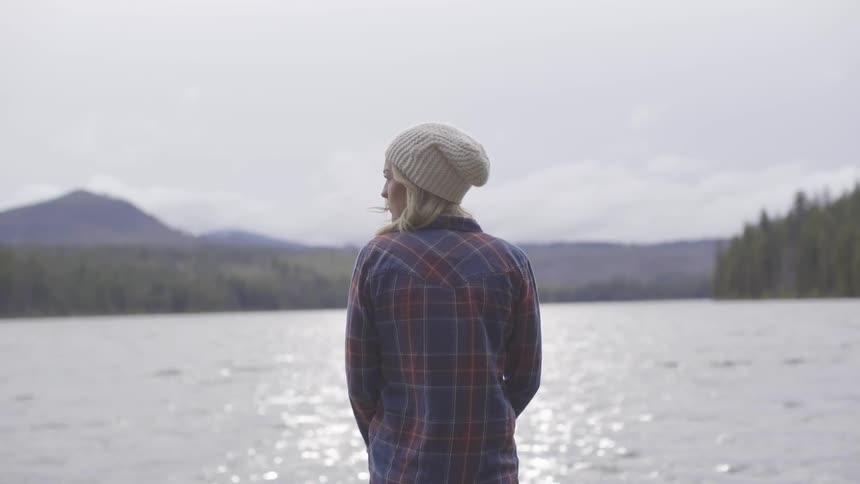A woman stands on the shore of a lake on a cloudy and breezy day
