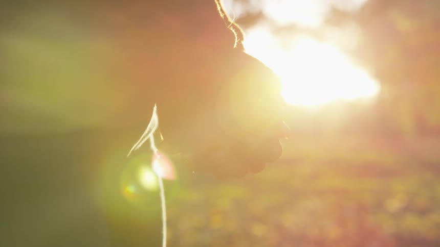 A woman stands still with clasped fingers in a field on an autumn day