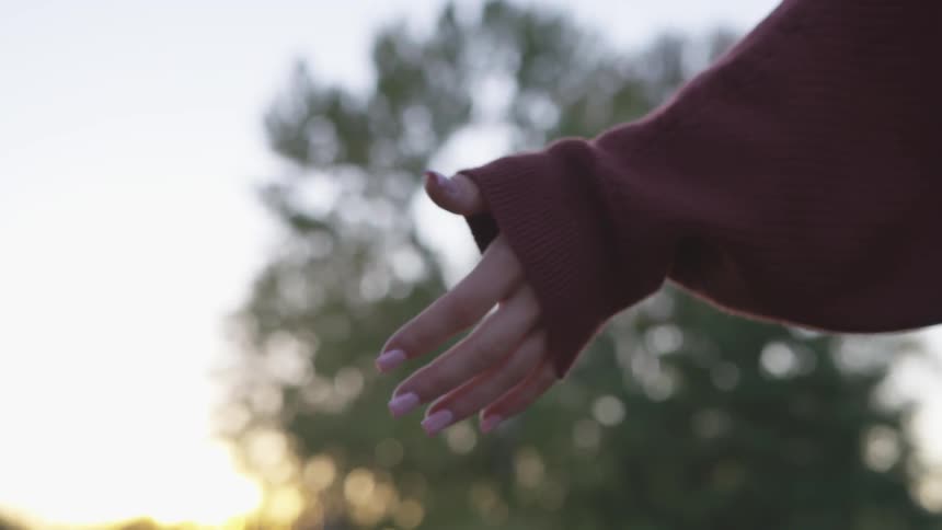 Woman holds her hand out in front of the setting sun