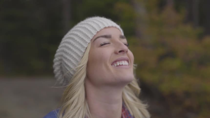 A young woman smiles with her eyes closed while standing in a wooded area
