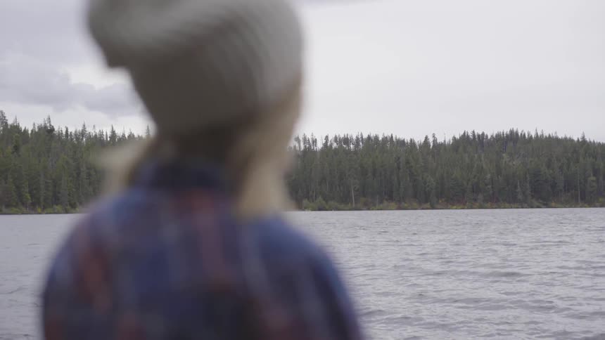 A blonde white woman stares across a lake