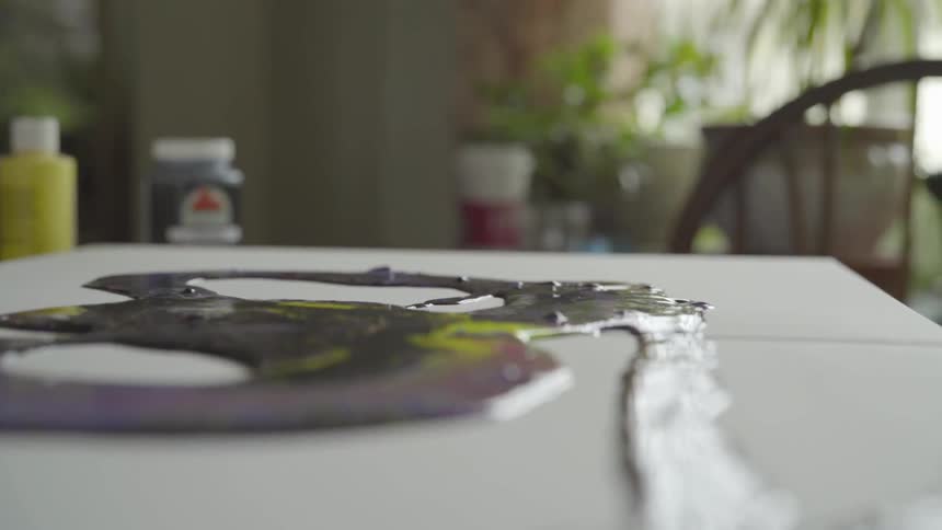 Person pours paint from jar onto canvas resting on table