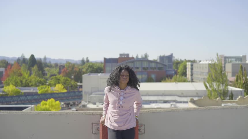 A young woman stands on a rooftop looking around on a sunny day