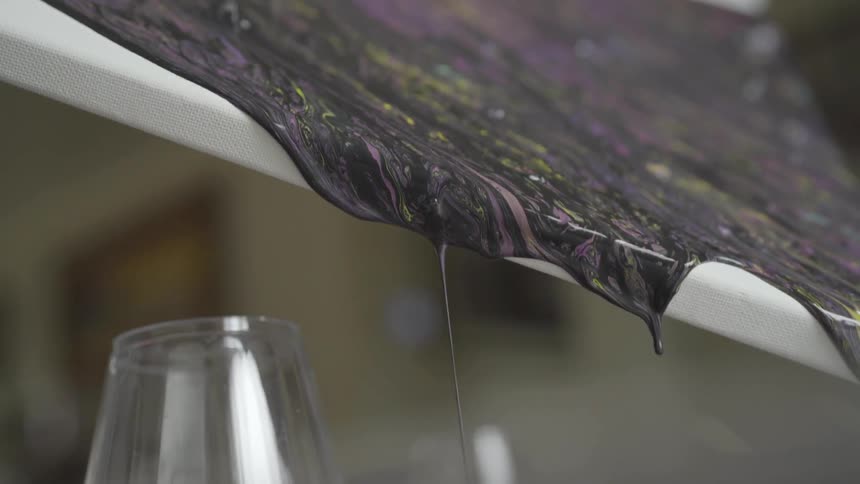 Multi colored swirled paint dripping off the edge of a canvas