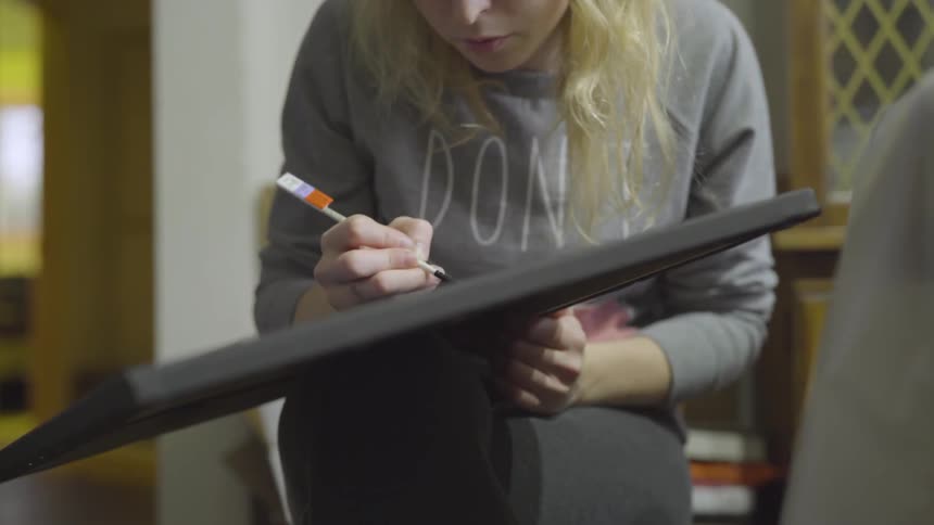 Woman paints on canvas held in her hands