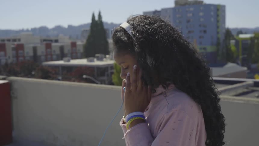 A young woman listens to music on her headphones while standing on a parking garage