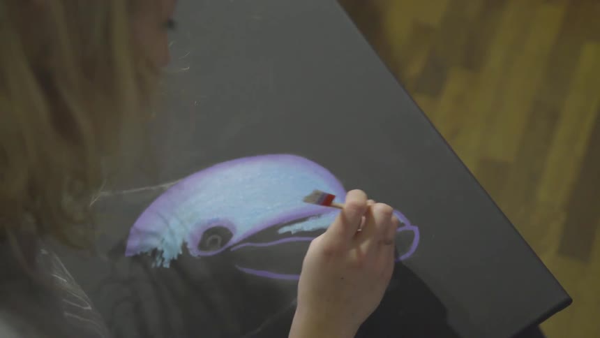A female artist paints a dolphin on a black canvas