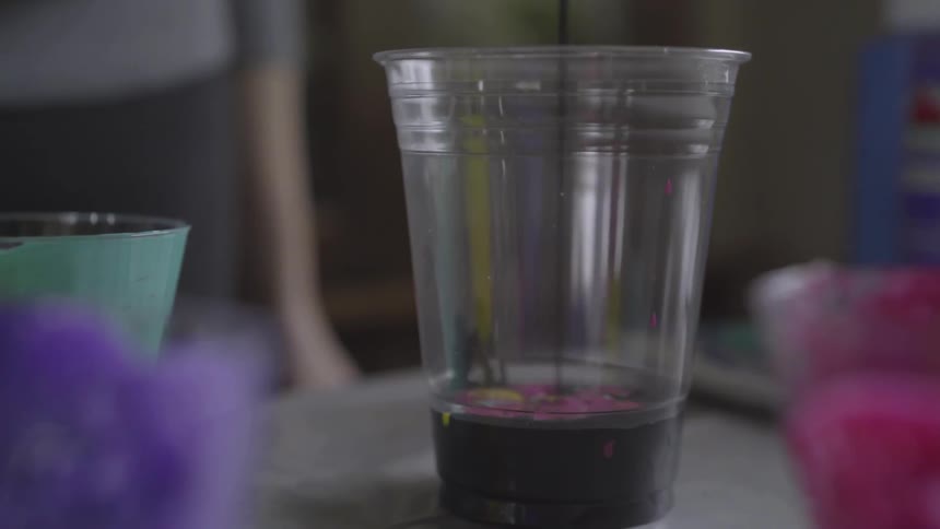 A clear plastic cup is being filled with purple paint