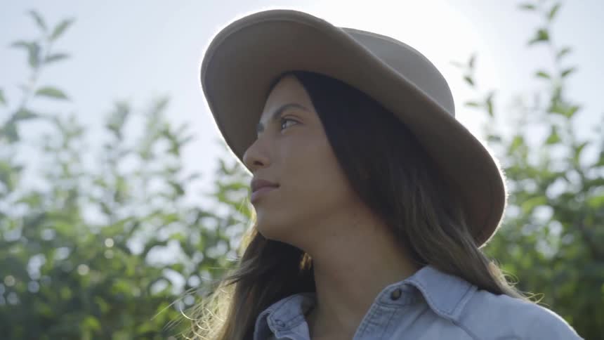 A young woman wearing a cowboy hat stands outside on a breezy day