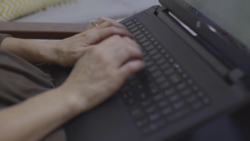 A female typing on a laptop propped on her lap