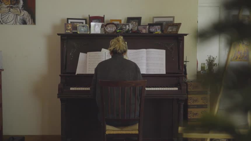 A blonde woman plays piano against a wall