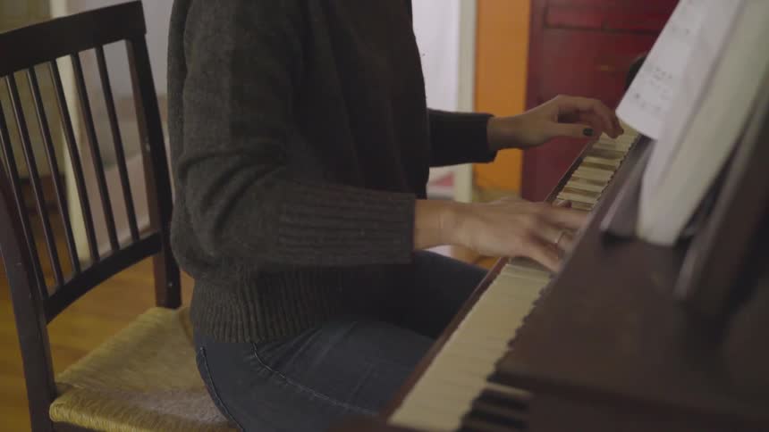 A blonde woman with glasses plays a piano in a living room