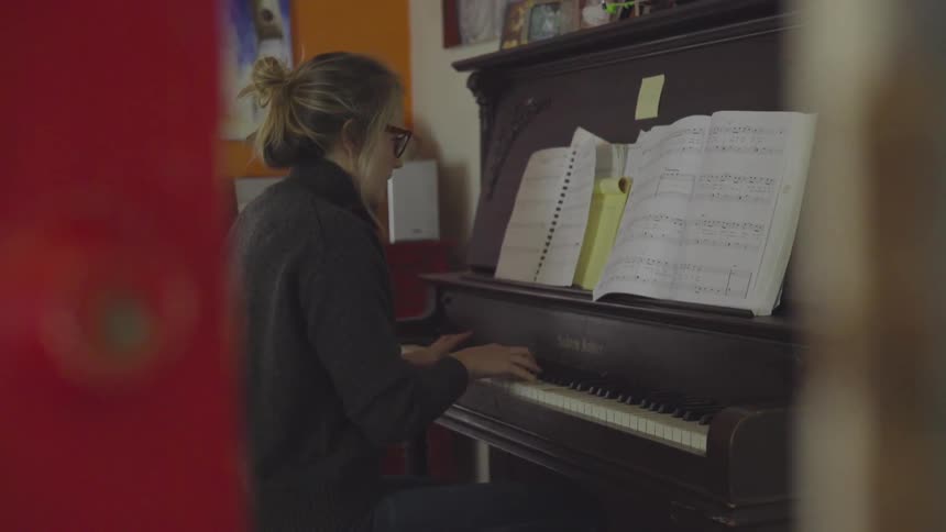 A woman playing an upright piano in a house