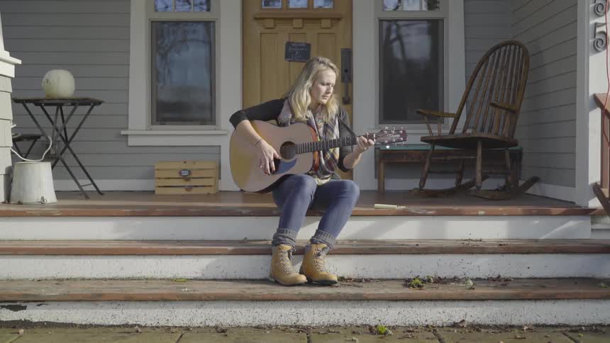 Woman sits on the steps to a house playing guitar