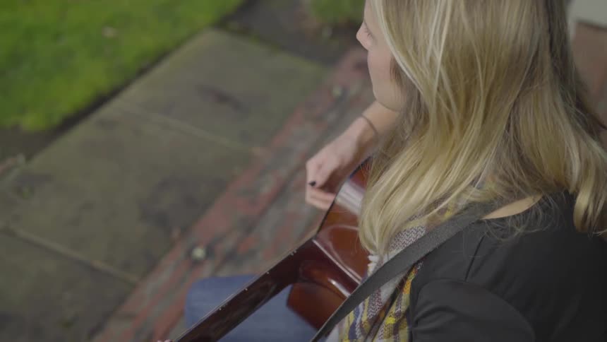 A woman playing the guitar while sitting outside