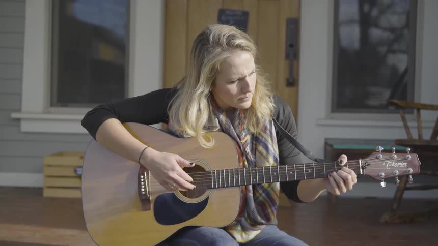 A white woman playing a guitar outdoors during the day