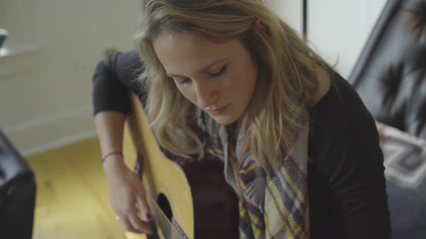 A female guitarist playing while sitting on a sofa indoors