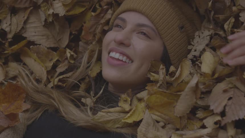 A woman smiles as she lays her head back down in a pile of fall leaves