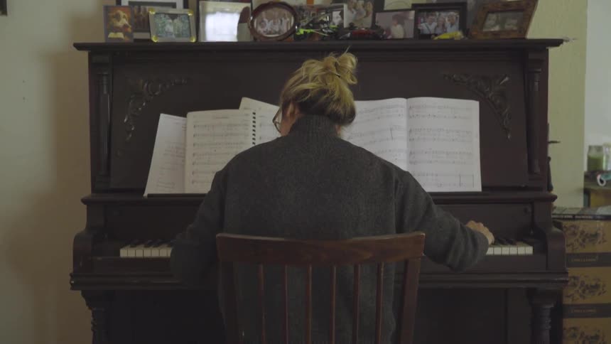 Back view of woman playing piano from sheet music