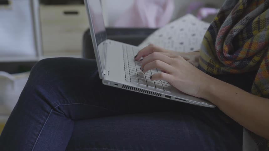 A woman types and sits cross legged with a laptop on her legs