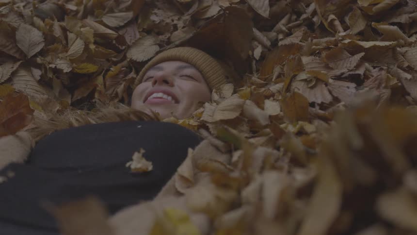A young woman smiles as she lays down while deeply nestled in a pile of fallen leafs