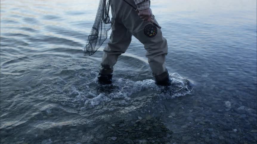 Person walks through shallow water carrying fishing equipment