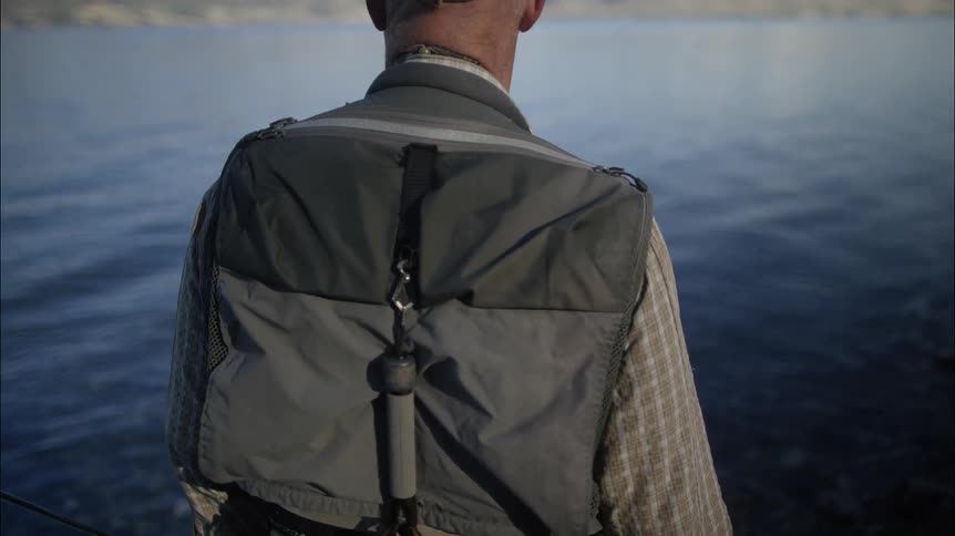 A fisherman stands along the shoreline holding his fishing pole