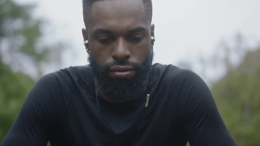 Black man sits down and listens to music with earphones in the forest by day